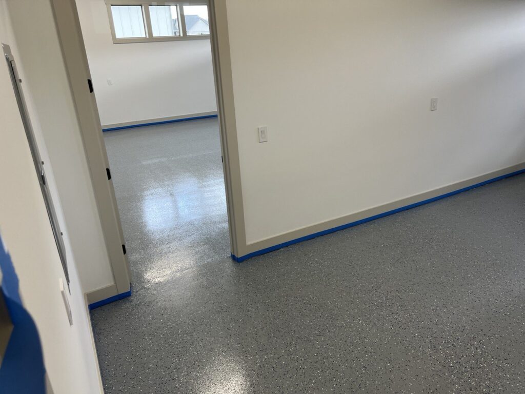 Empty room with white walls and speckled epoxy floor.